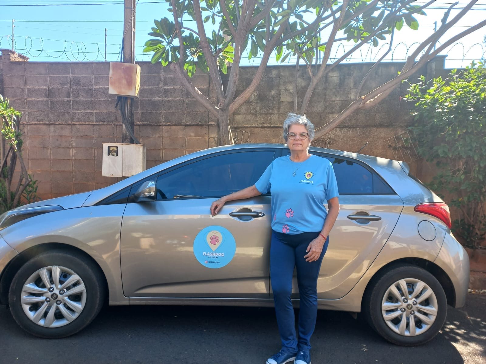Flashdoguer ao lado do carro adesivado, sorrindo